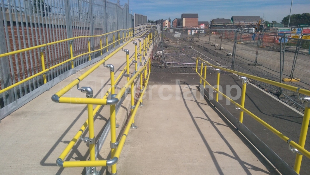 Interclamp Key Clamp DDA Assist fittings and safety yellow powder-coated handrail tube providing a sturdy and highly visible handrail for a disabled access ramp at a busy train station.